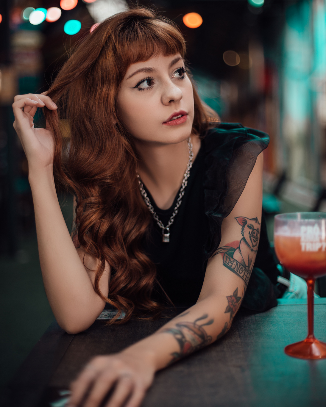 Beautiful Young Woman in Black Blouse Leaning Forward on a Wooden Table Holding Her Hair